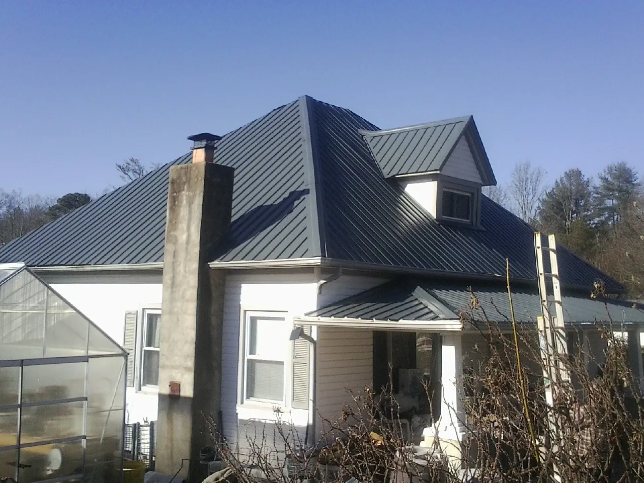 Dark blue standing seam metal roof on a white farmhouse with dormer — Slate & Tile Roof Repair by Roofing Brothers in Saint Maries