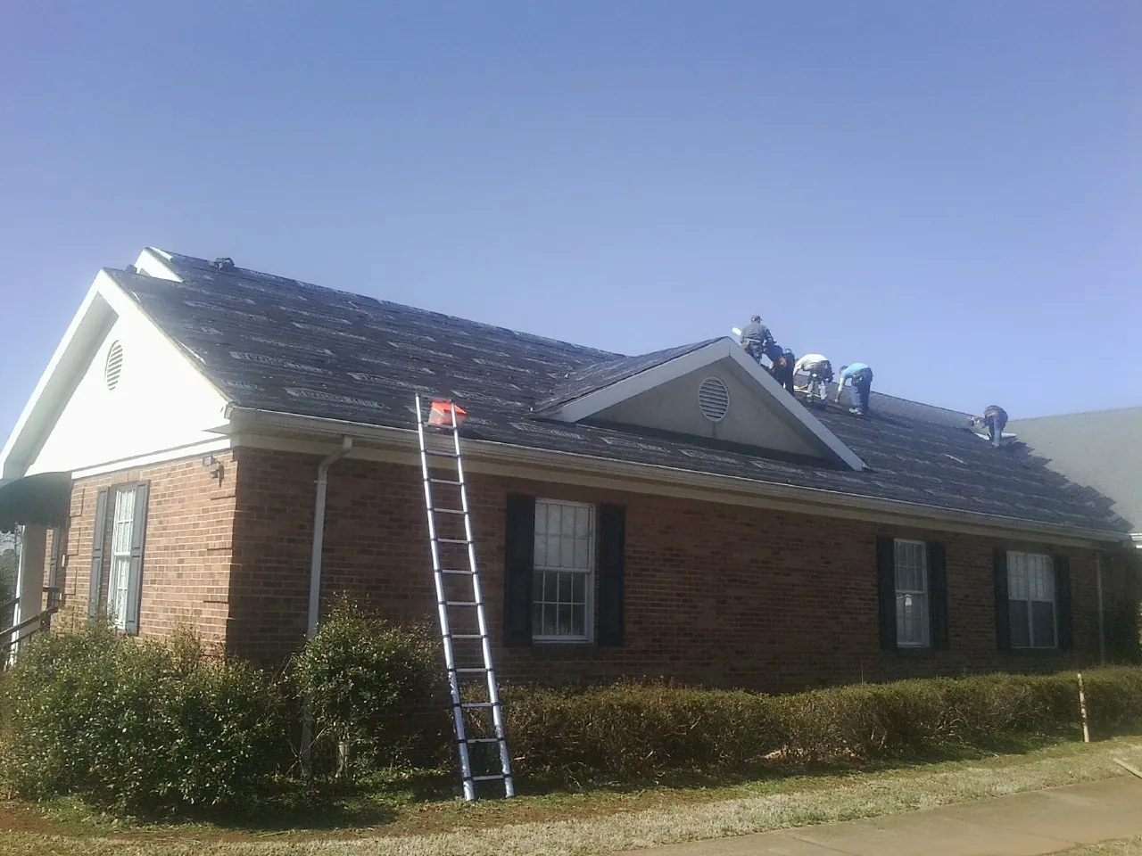 Crew tearing shingles off a brick ranch roof with a ladder set — Metal Roof Repair work by our crew in Saint Maries