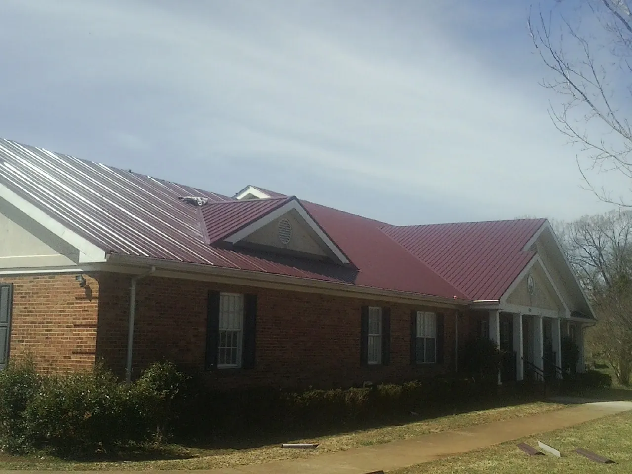 Red metal roof with gabled entries on a long brick building, from a Hail Damage Roof Repair job in Saint Maries