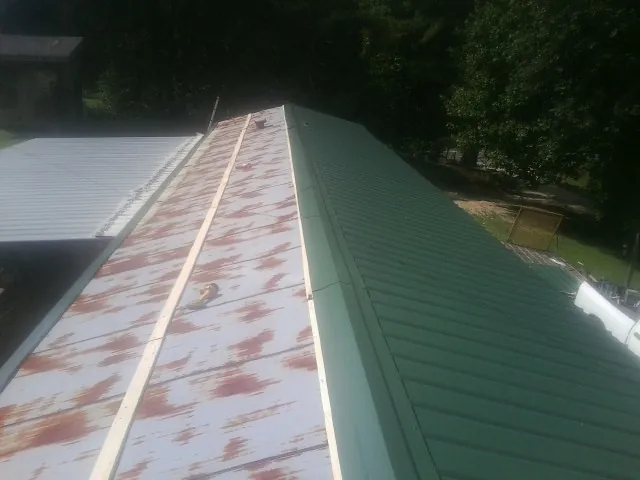 Old rusted panels beside newly installed green metal roofing — Wind Damage Roof Repair by Roofing Brothers in Saint Maries