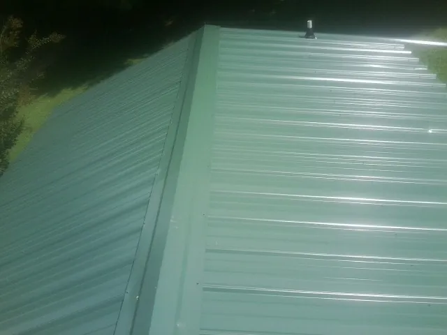 New green metal panels meeting at the ridge of a roof — Flat Roof Repair work by our crew in Saint Maries