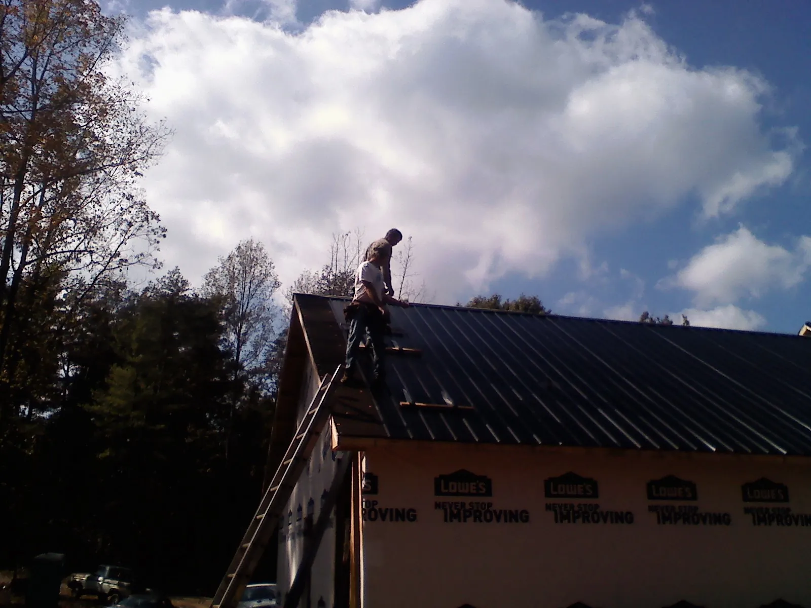 Roofer fastening dark metal panels high against a cloudy sky, from a Roof Inspection job in Saint Maries