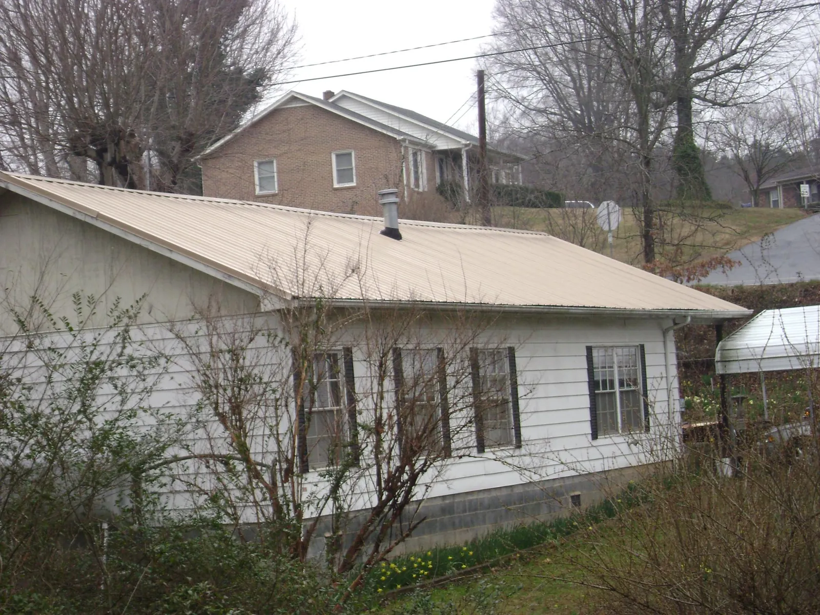 Tan metal roof on a white sided house set into a hillside — Commercial Roofing by Roofing Brothers in Saint Maries